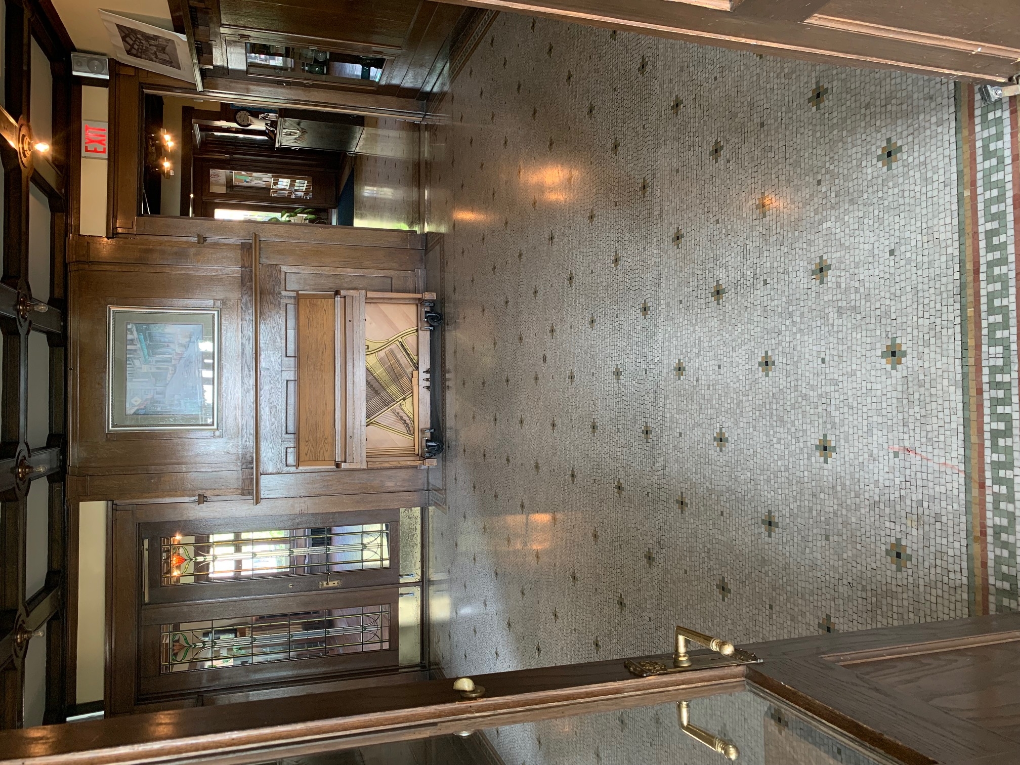 Grand entryway with mosaic tile floor and wood-paneled walls. A piano sits by the wall.